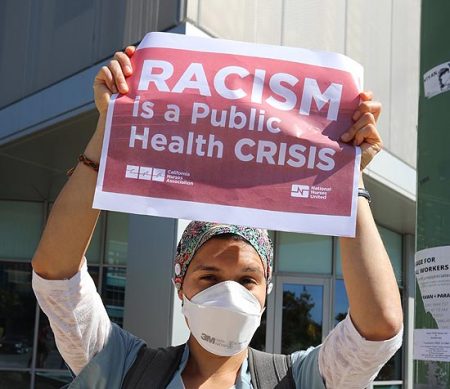 nurse holding racism health crisis sign