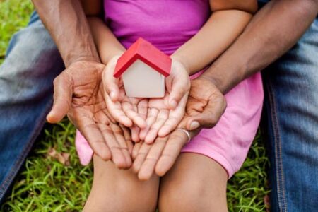 Hands holding a small house in green park