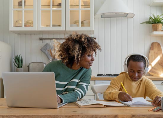 Black student studies while mother looks on.