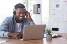 Young Black man smiling while working in front of a laptop computer.