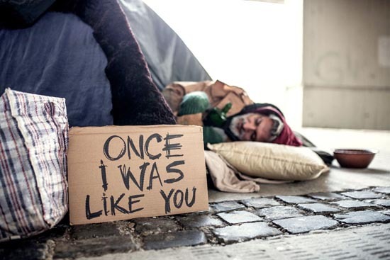 Homeless person sleeping on the street behind a sign that reads "Once I was like you."