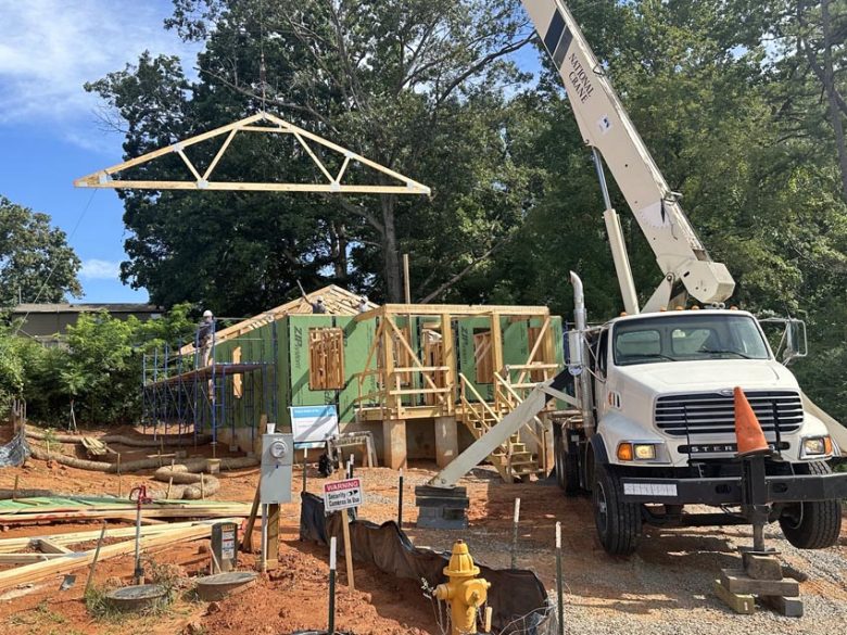 A crane lowers a roof truss onto a Habitat home.